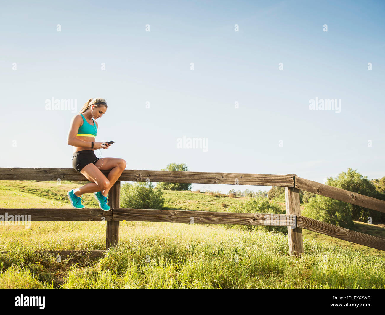 woman-sitting-on-fence-using-smart-phone-EXX2WG.jpg