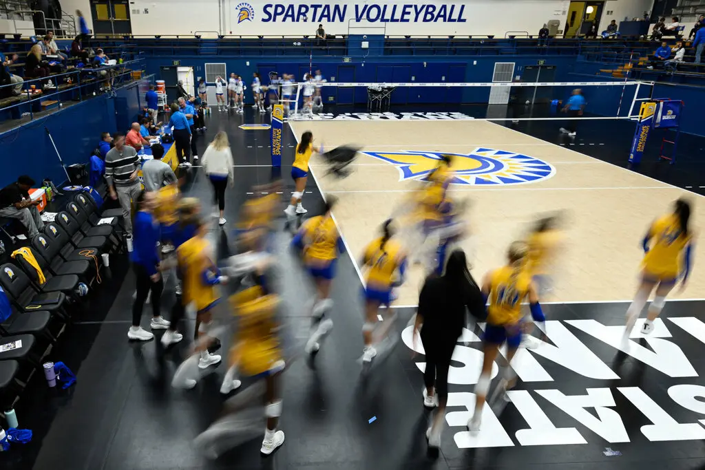 Several volleyball players, in yellow and blue uniforms, stand around a volleyball court.