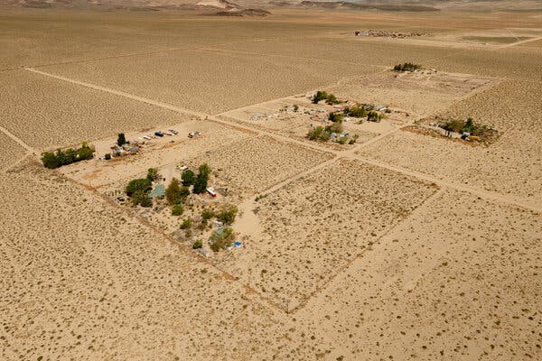 An aerial view of a desert-like landscape with a few houses in view.