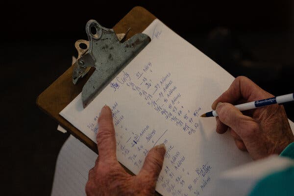 Hands are seen writing a list on a clipboard.