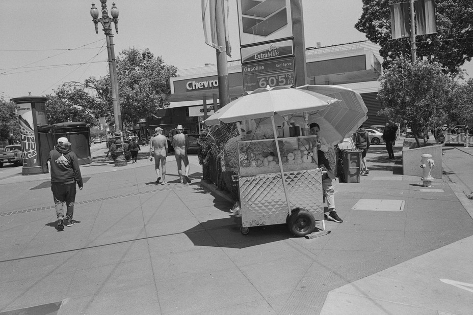 a street scene with two men nude walking past a food vendor