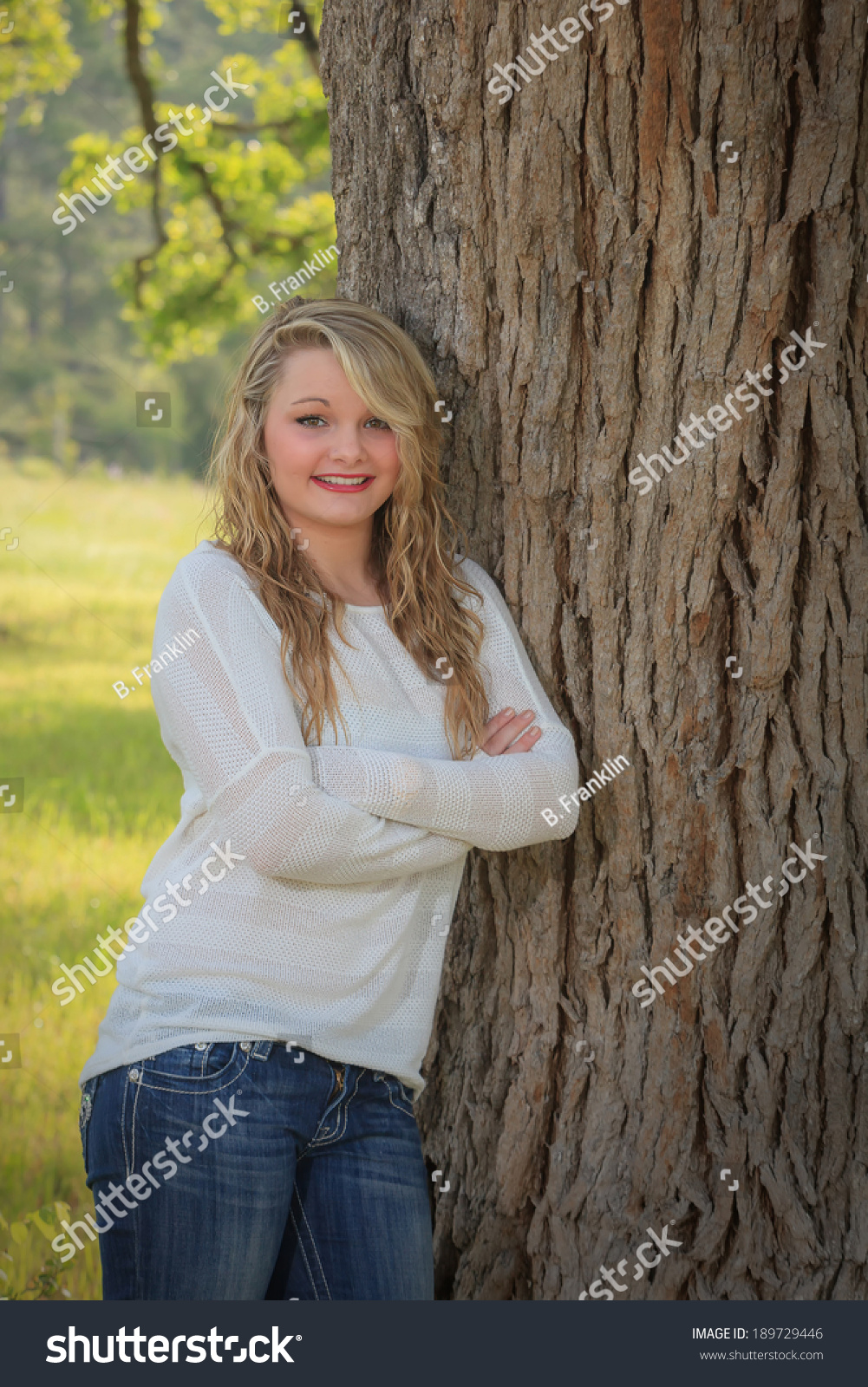 stock-photo-pretty-teen-girl-leaning-against-oak-tree-wearing-long-sleeve-white-sweater-and-blue-jeans-189729446.jpg