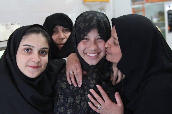 A group of four women in dark head coverings. One woman is kissing the cheek of Caroline Kristof.