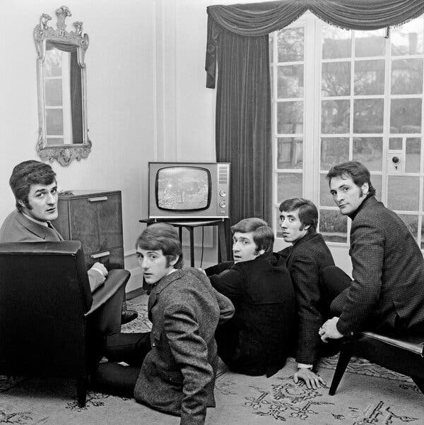 A black-and-white photo of five well-dressed young men sitting around a small TV set in a house. Their backs are to the camera, but they are looking at it over their shoulders.