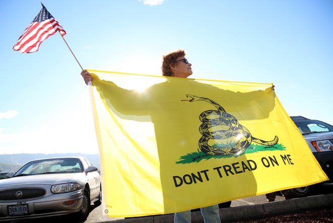 Leslie Corp holds up an American flag and the Gadsden flag while waiting outside of Roseburg Municipal Airport for President Barack Obama's arrival in Roseburg, Oregon, on Friday, Oct. 9, 2015. Gun-rights activists say they planned to protest potential gun restrictions when Obama visited. (AP Photo/Ryan Kang)