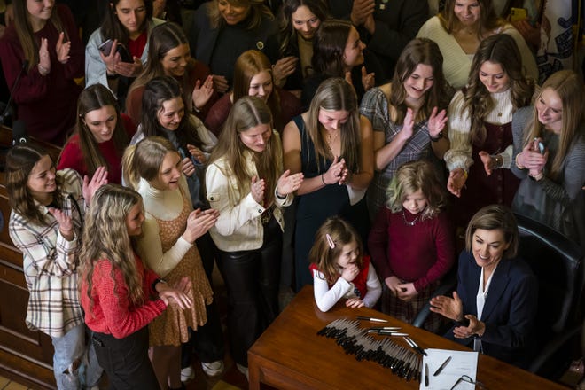 Gov. Kim Reynolds, surrounded by female athletes, signs House File 2416 into law, prohibiting transgender women and girls from competing in female sports offered by Iowa schools, colleges and universities, on Thursday, March 3, 2022, in the rotunda of the Iowa State Capitol, in Des Moines.