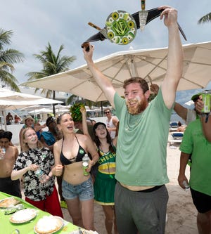 Joshua Mogle, right, of Altoona, Iowa, raises the winner's belt after devouring a 9-inch Key lime pie at the World Famous Key Lime Pie Eating Championship Tuesday, July 4, 2023, in Key West, Florida. Mogle, a 38-year-old tire manufacturing manager, consumed the Florida Keys' signature dessert in three minutes and 35 seconds, the fastest time of 25 contestants.